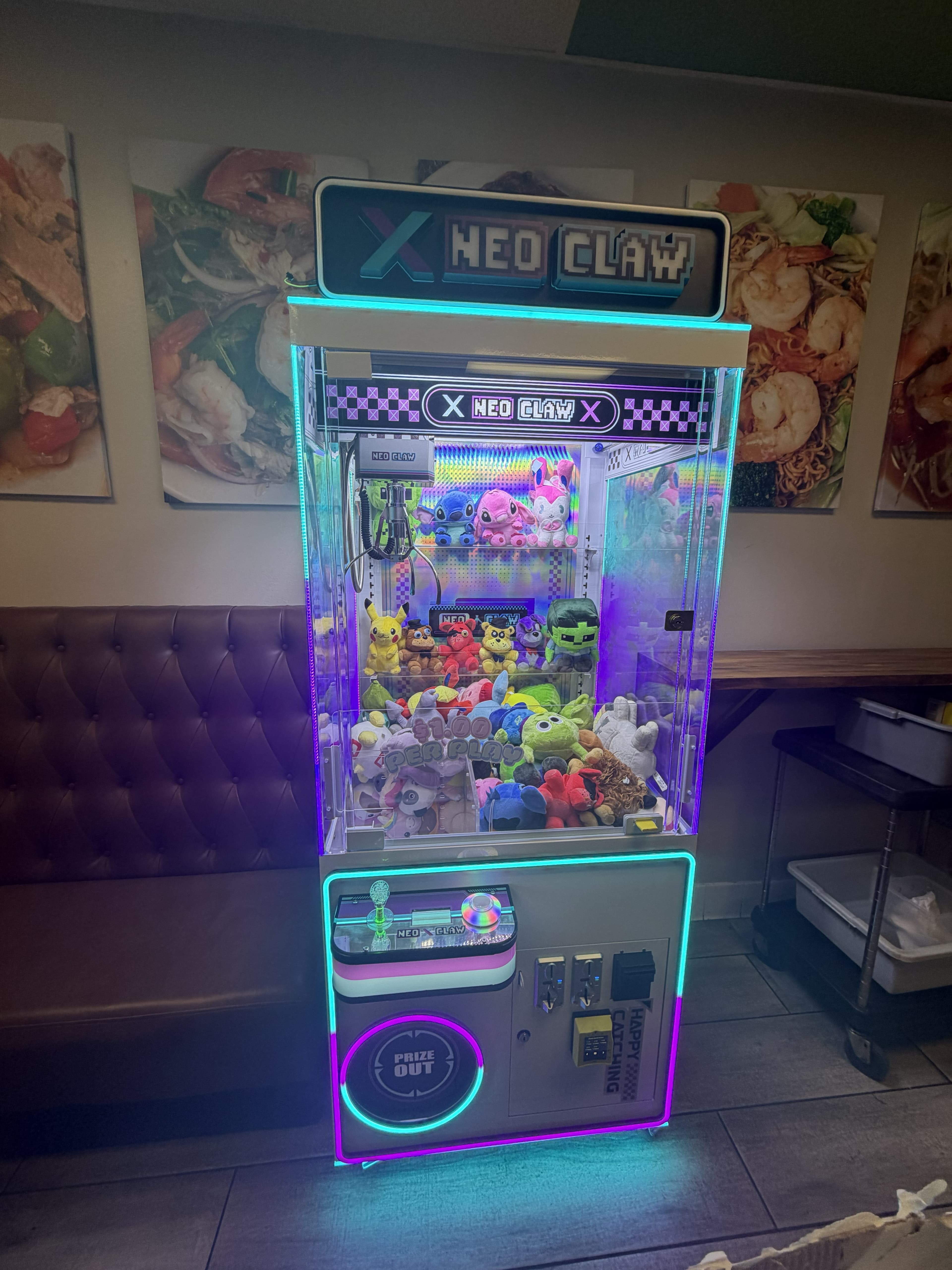 A neon-lit Neo Claw machine filled with colorful plush toys in a restaurant setting.