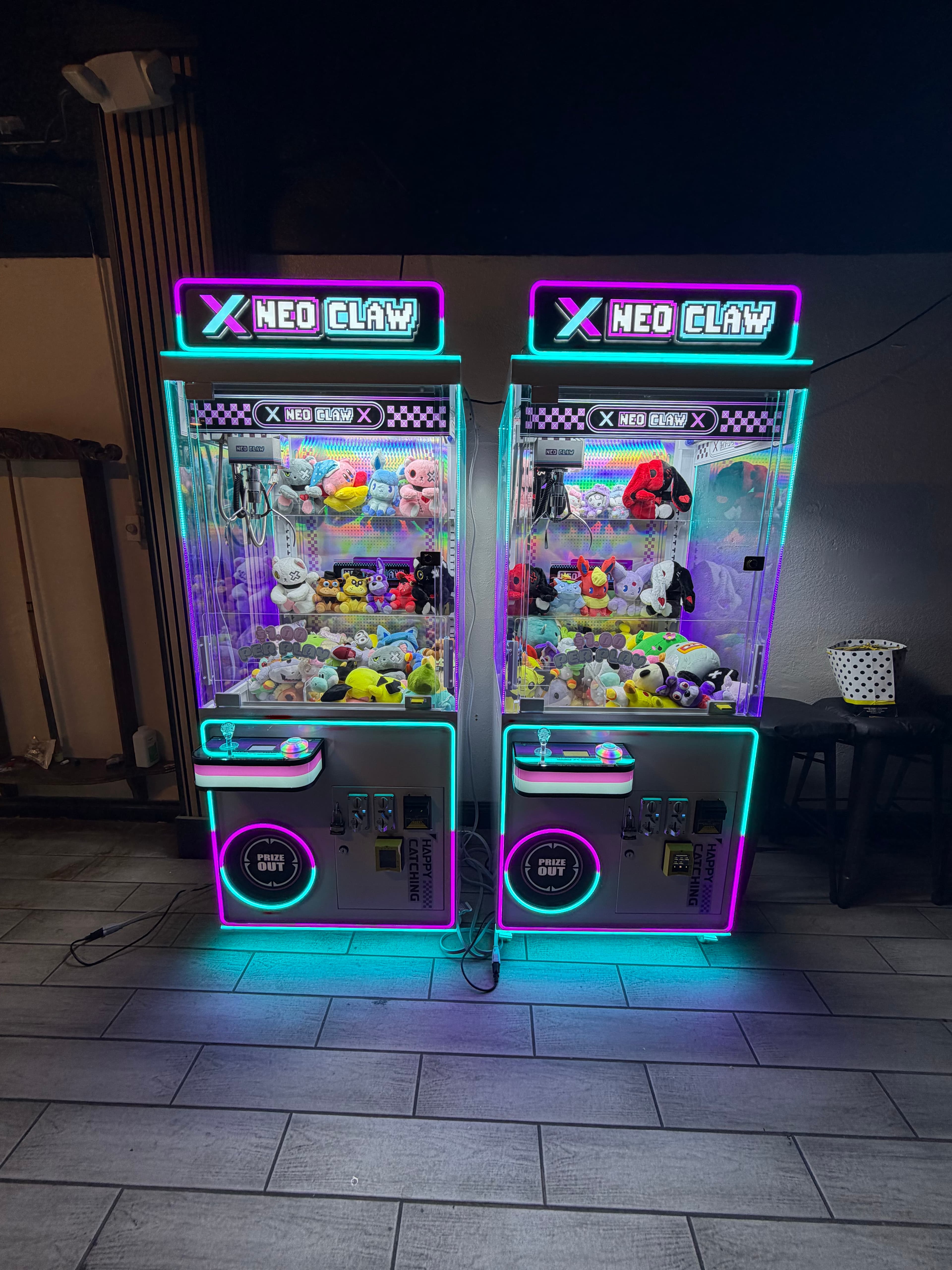 Two Neo Claw machines glowing with cyan and magenta neon lights, filled with plushies.