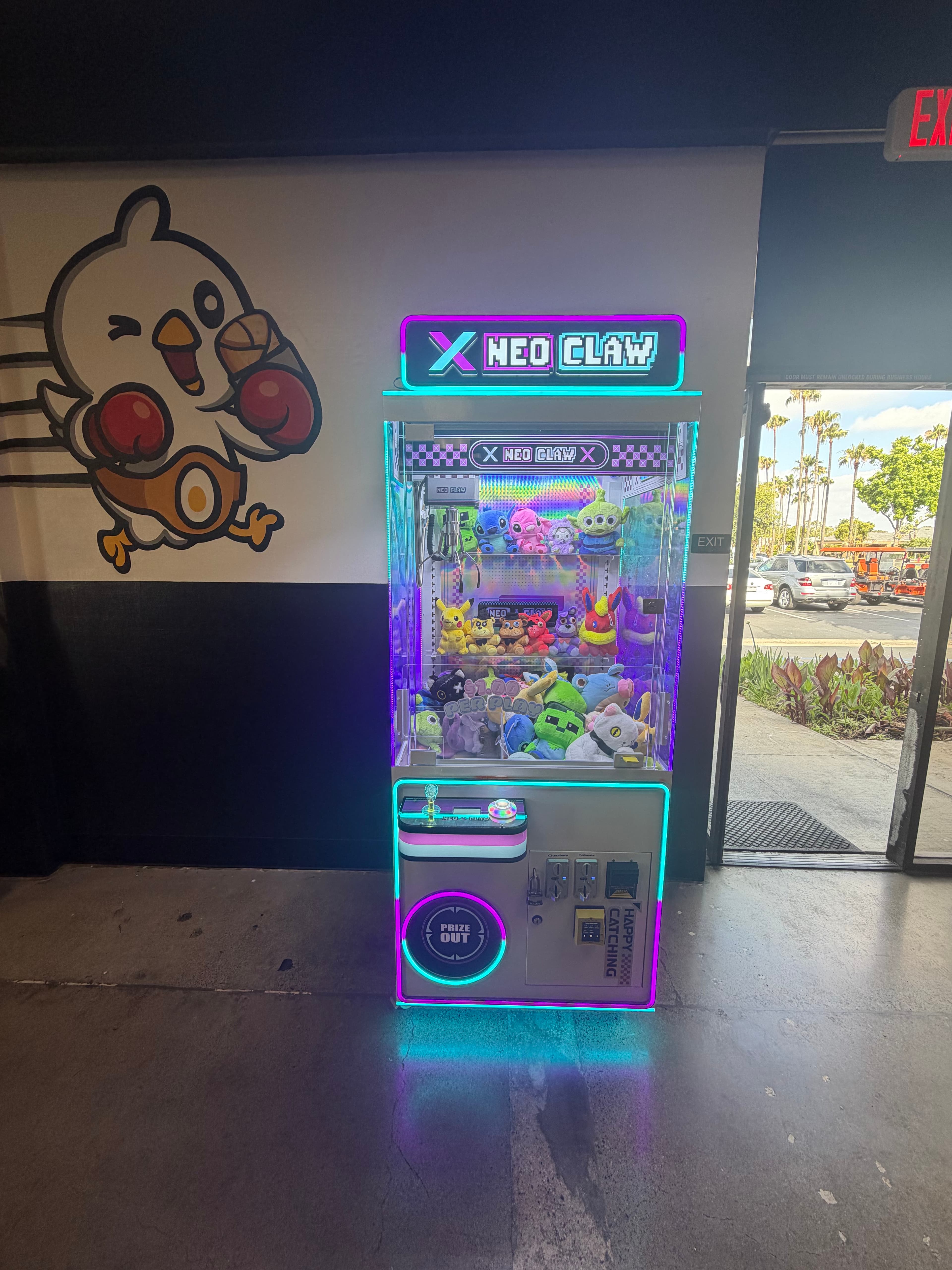 Neon-lit Neo Claw machine filled with plush toys next to a cartoon chicken wall mural.
